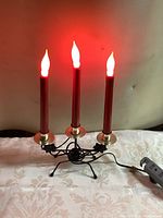 Electric candelabra with three lit red candle-shaped bulbs on brass holders and a black metal stand.