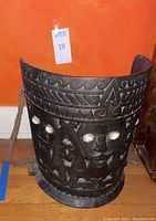 Front angled view showing carved faces, shell inlay eyes and rope handle