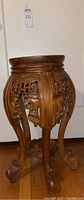 Full view of the intricately carved wooden side table showing round top and curved claw-foot legs.