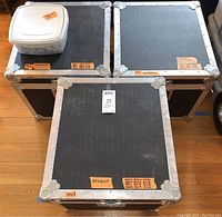 Three Wilson black metal reinforced storage/travel cases on floor, metal edged, labeled with contents and sizes