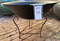 Side view of black metal fire pit bowl on rusted iron stand on brick surface.