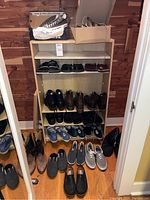 Wooden shelving unit holding multiple pairs on shelves and floor in front