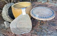 Overview photo showing all items together outside on a brick surface: ceramic planter, granite bowl, serpentine stone slab, mosaic tile table with iron legs.