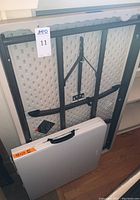 Folded view of both tables showing white tops and black folding legs; smaller table has handle.