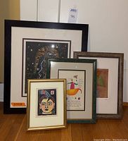 Four framed art prints grouped on floor: largest black frame, gold frame, teal patina frame and wood-tone frame visible
