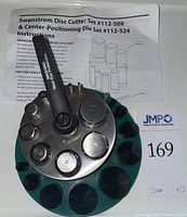 Overall top-down view of disc cutter and conical dies in green foam holder, with instruction sheets and rotary handle.