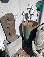 Overview showing Buddha statue on cinderblocks next to glazed ceramic pot and metal garden stakes