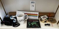 Photo of a shelf with a white Apple mug, rolled tech history poster, trade show lanyards, CD case, and a brass Hewlett-Packard round box with lid