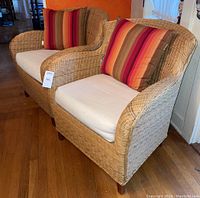 Front view of two wicker chairs with off-white cushions and striped pillows, showing their size and condition.