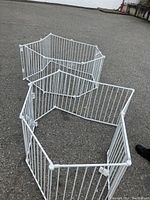 Overview of white metal alloy steel configured baby gate and fence panels arranged on ground forming hexagonal containment area.