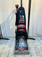 Front view showing upright vacuum cleaner with clear water compartment and visible labels about brush rows and power rating.