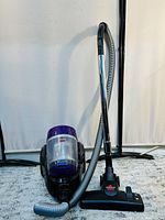 Full view of BISSELL PowerForce bagless canister vacuum cleaner showing the hose, wand, and floor brush attachment on a light carpet.