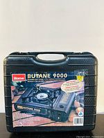 Closed black plastic carrying case with labeling showing the Home Butane 9000 portable gas stove for indoor/outdoor use, in like-new condition as per seller.