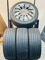 Four Michelin Pilot Sport A/S 3+ 245/45 ZR20 tires stacked in front of a single mounted multi-spoke rim on stand