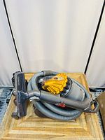 Dyson DC23 canister vacuum cleaner coiled with hose and floor tool attachment laid on wooden surface.