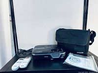 Top view of projector with cables, two remotes, carrying bag and user manual arranged beside it