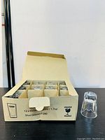 Box containing 12 Finlandia shot glasses, showing glasses wrapped in protective packaging with one glass placed outside to view design.