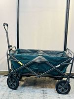 Side view of heavy duty folding wagon showing green fabric and black metal frame with large wheels and pull handle