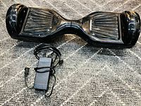 Top-down view of black hoverboard with charger placed below it, showing overall condition and included charger.