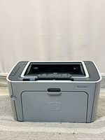 Front view of the HP LaserJet P1505 printer showing power button on left, output tray on top, and HP logo on front panel.