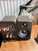 Front and rear view of two Kanto YU2 mini speakers placed side by side showing front speaker cones and rear input/output connections and branding.