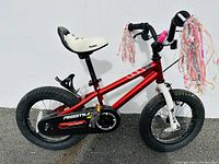 Side view of red kids bike with white seat, black tires, and handlebar streamers.
