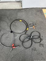 Four flexible steel cables of various lengths with double loop ends arranged on pavement. Includes identification tags and colored protective sleeves on loops.