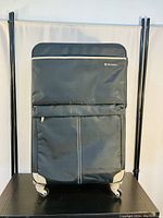 Front view of black Monroza suitcase showing front zippered compartments and four wheels.