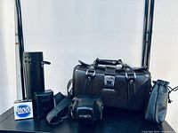 Full view of all items included in the lot: Olympus leather camera bag, Minolta camera in case, cylindrical lens case, smaller pouch, drawstring pouch, and box.