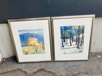 Two medium framed paintings showing autumn tree landscapes against blue mountain backgrounds.
