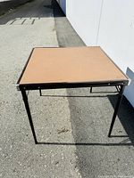 Full view of the portable card table showing the flat top and legs set up outdoors.