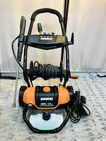Front view of WORX electric pressure washer with hose on reel and metal wand on stand, placed on carpet.