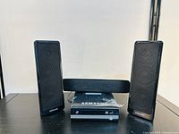 Front view of Samsung multi DVD recorder with three Samsung speakers arranged around it on a black surface.