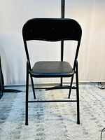 Front view of a black folding chair with padded seat and backrest on a grey carpet.