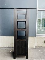 Front view of tall dark wooden shelf unit showing three open shelves and closed bottom storage compartment.
