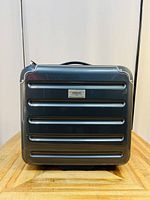 Front view of black Torrente suitcase showing horizontal ridges and brand logo plate.