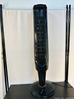 Front view of the black tower fan showing the tall and slim design with a grille panel and circular base