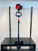 Full view of the Troy-Bilt 27cc weed wacker standing upright on a black table against a neutral background, showing the straight shaft and loop handle.