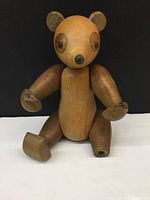 Front angled view of mid century wooden bear figurine showing natural wood tones, rounded ears, eyes, nose, articulated arms and legs, and missing right front paw.