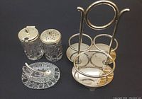Full view of the cruet set including cut glass containers with lids, small glass tray, sterling spoon, and silver-tone stand with handle.