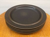 Stacked view of six dark brown speckled stoneware plates showing the upper side with concentric circular design and textured glaze.