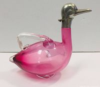 Front and side view of cranberry glass decanter shaped like a duck with silver neck and beak detailing, showcasing the smooth glass handle and overall shape.