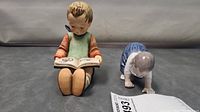 Two ceramic figurines together, Goebel Hummel child reading and Royal Copenhagen crawling baby