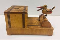 Side view of wooden automated cigarette dispenser with duck figurine on rotating mechanism and dog inlay on lid
