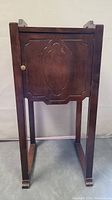 Front view of vintage walnut side table with single door featuring carved design and brass knob, legs and feet visible.