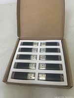 Top view of the open box containing ten black USB sticks with transparent caps.