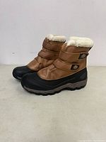 Side view of the brown and black men's boot with white fur lining and velcro straps.