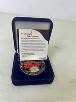 Close-up view of commemorative coin in blue velvet display box, showing the coin's design and accompanying certificate.