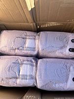 Four packs of Depend pull-up style adult diapers in white, size large, absorbency level 4, in original plastic packaging inside a cardboard box.