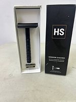 Front view of the matte black Henson Shaving AL13 aluminum safety razor in its white box alongside the black outer packaging showing brand and product details.